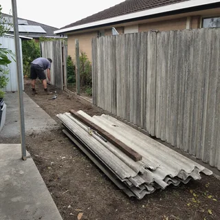 Old grey fibre cement boundary fence partly removed in a suburban backyard