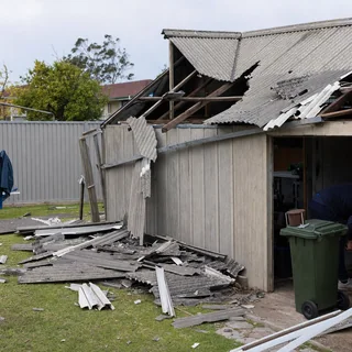 Storm damaged fibre cement shed roof with broken sheets in a backyard