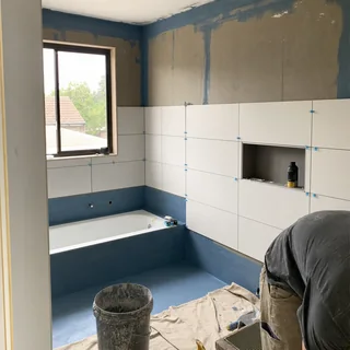 Newly tiled bathroom wall and floor with waterproofing membrane visible in the shower recess