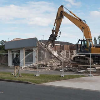 Large industrial warehouse being demolished by a high reach excavator
