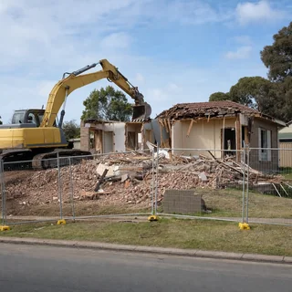 Excavator demolishing a single storey brick house on a suburban block