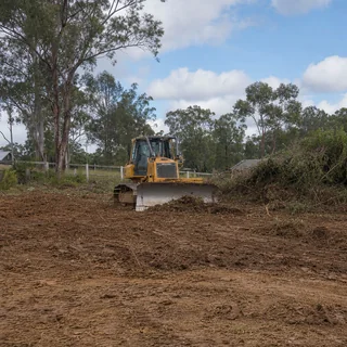 Cleared and levelled rural block with an excavator and stockpiled vegetation