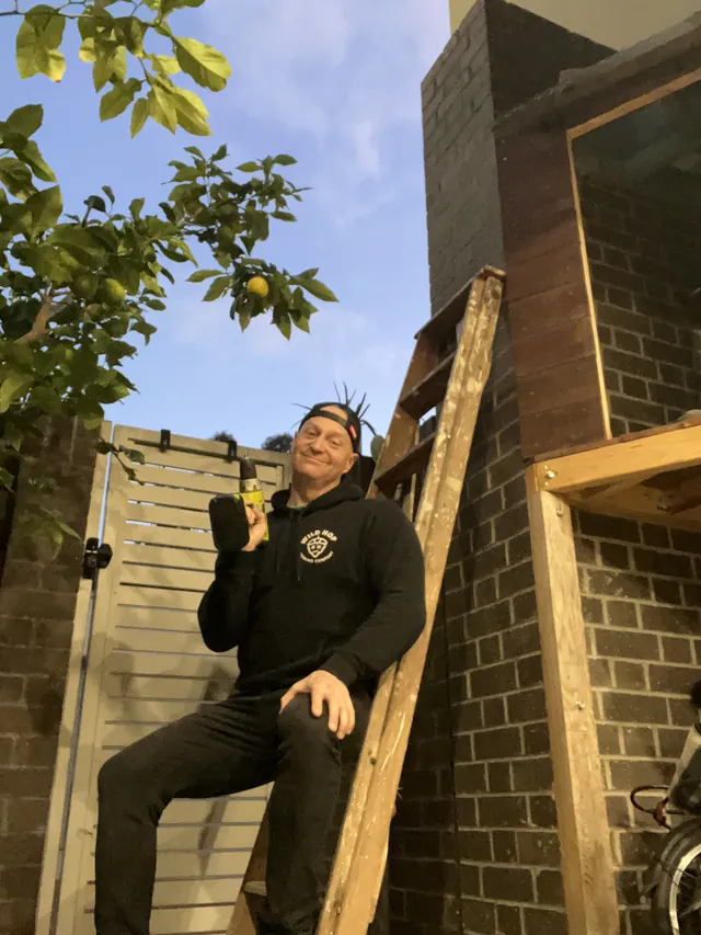 Levi Saunders from The Lead Gen Lab holding a cordless drill outside a brick house.