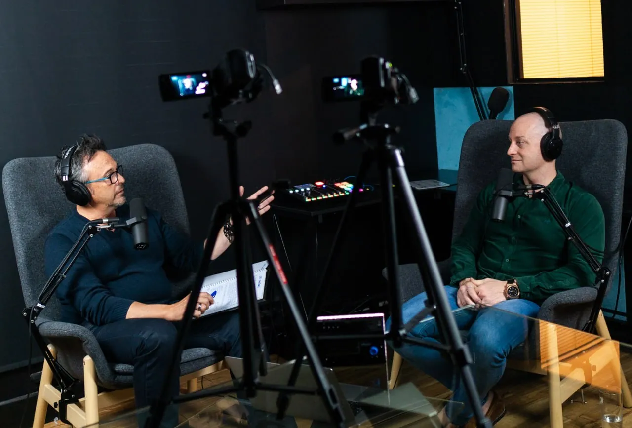 Levi Saunders, right, in a green shirt and headphones, talking with Dave in a recording studio with two cameras on tripods