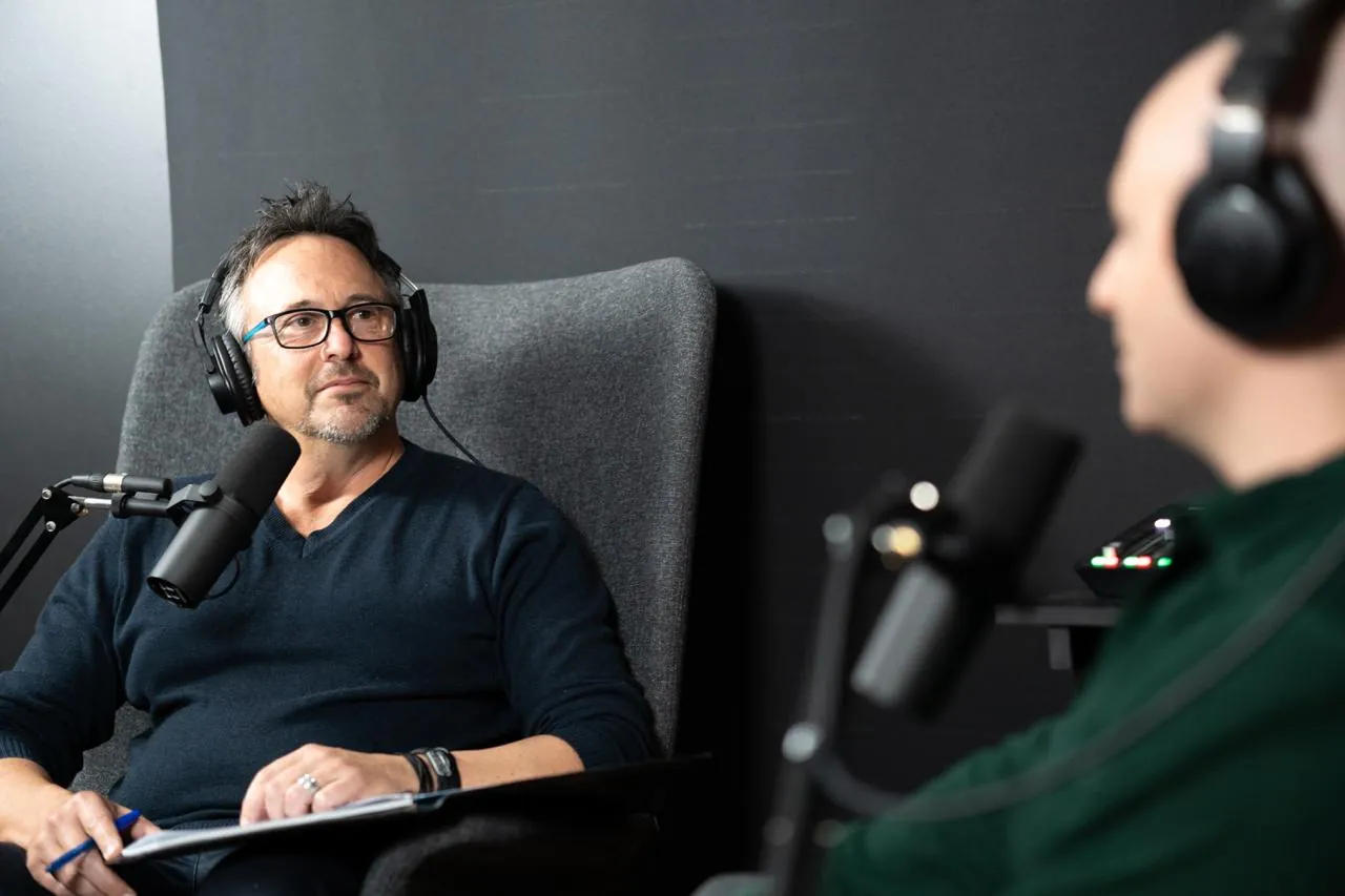 Dave in a studio chair with headphones and a microphone, talking with Levi Saunders, who sits on the right