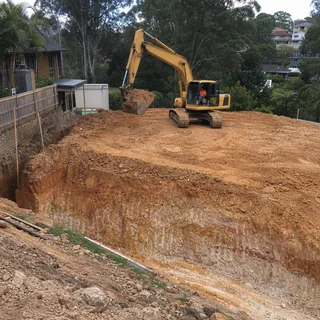 Excavator cutting and levelling a building pad on a residential block