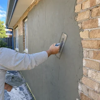 Smooth grey cement render being applied to an exterior brick wall