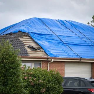 Storm damaged roof with broken tiles and a temporary tarp fitted