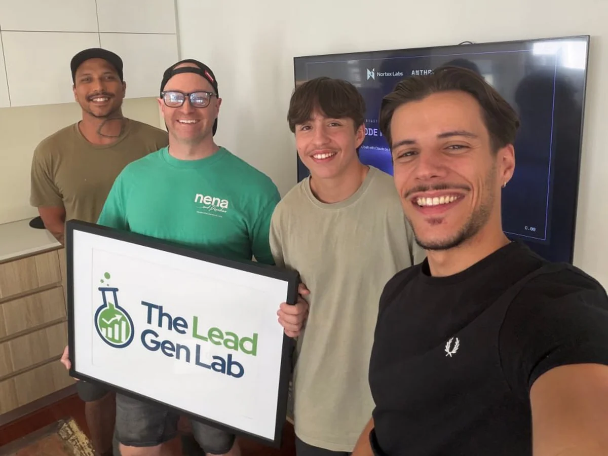 Four men smiling at the camera in a kitchen and office space, one of them holding a framed Lead Gen Lab logo, with a presentation screen behind them.