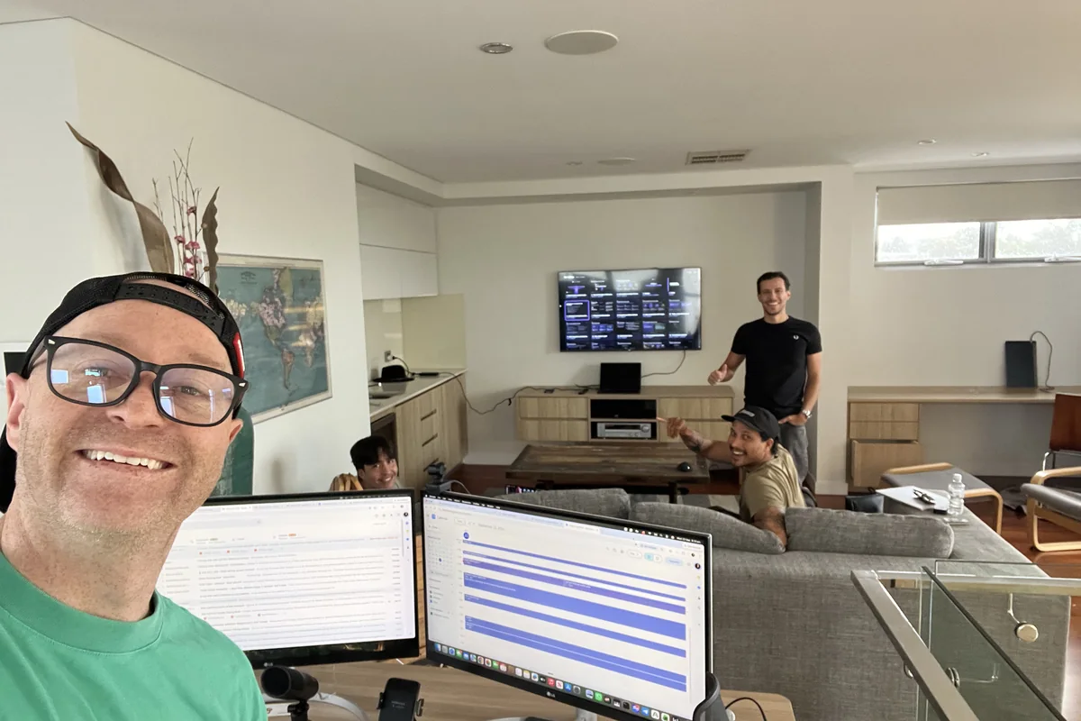 Four people working in an open plan office, two at a desk with monitors showing an inbox and a calendar, two more talking beside a couch and a wall mounted screen.